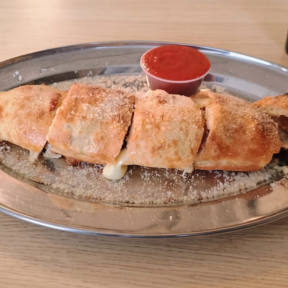 A sliced stromboli with melted cheese and parmesan on a metal plate with a side of marinara sauce.